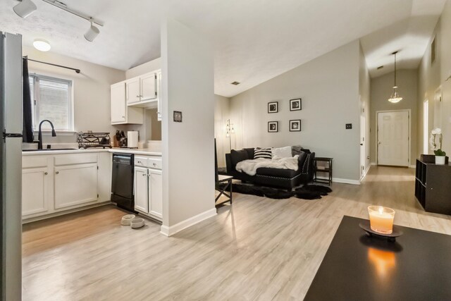 kitchen featuring lofted ceiling, black dishwasher, light wood-style flooring, and a sink