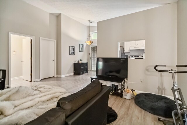 living room featuring high vaulted ceiling, light wood-style flooring, and baseboards