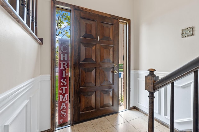 entrance foyer featuring a decorative wall, light tile patterned floors, a wainscoted wall, and stairway