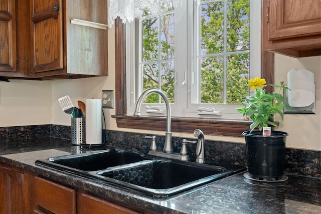 kitchen featuring a sink, dark stone counters, and brown cabinets