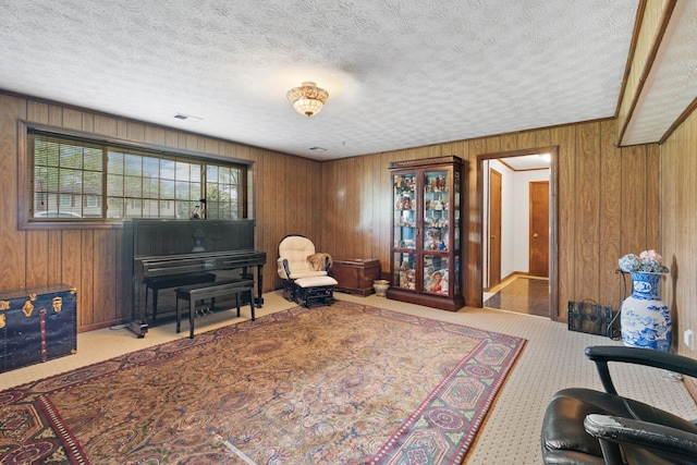 living area with wooden walls, a textured ceiling, and visible vents