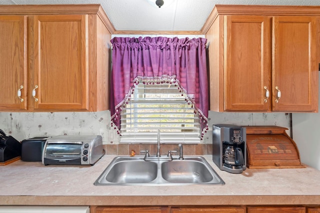 kitchen with a toaster, brown cabinetry, light countertops, and a sink
