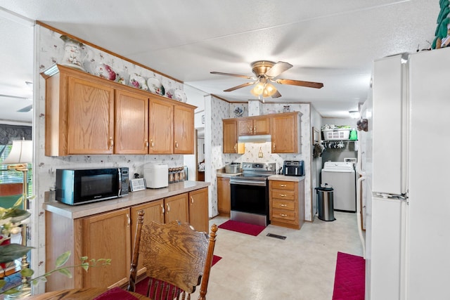kitchen featuring black microwave, stainless steel range with electric stovetop, freestanding refrigerator, under cabinet range hood, and washer / dryer