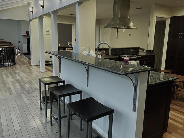 3426 Pepperhill Rd, Lexington, KY 40502 - kitchen with island exhaust hood, decorative columns, dark stone countertops, and light wood-type flooring