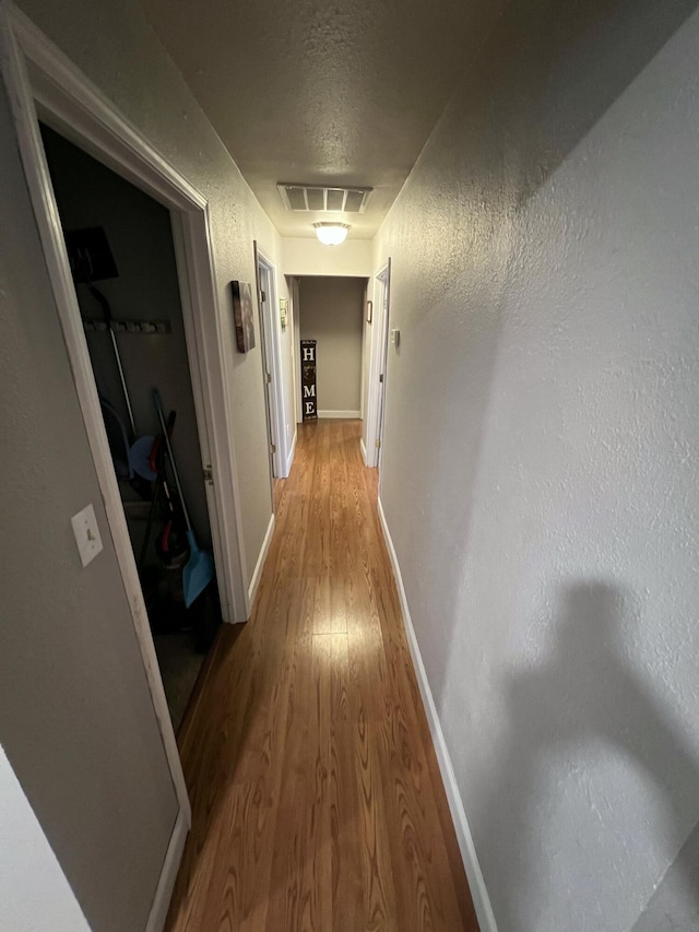 corridor with attic access, light wood-type flooring, visible vents, baseboards, and a textured ceiling