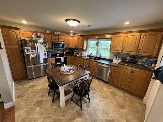 kitchen with brown cabinetry, appliances with stainless steel finishes, dark countertops, a sink, and visible vents