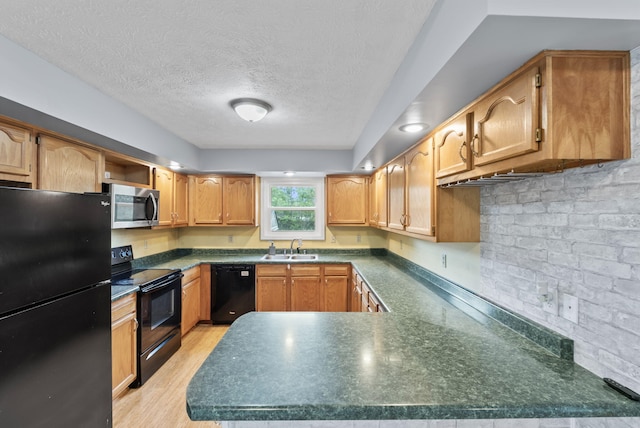 kitchen with a peninsula, dark countertops, a textured ceiling, a sink, and black appliances