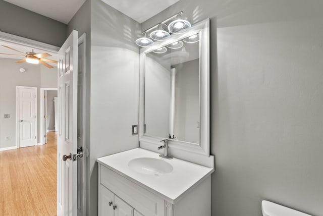 half bathroom featuring toilet, a ceiling fan, wood finished floors, and vanity
