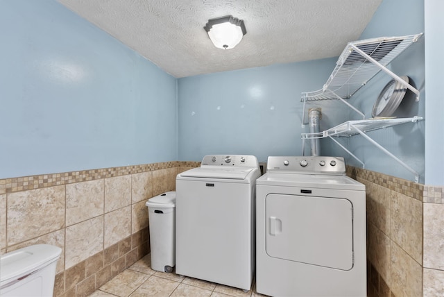 laundry area featuring laundry area, wainscoting, tile walls, a textured ceiling, and separate washer and dryer
