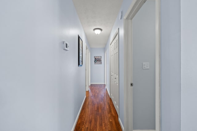 hallway with a textured ceiling, baseboards, and wood finished floors