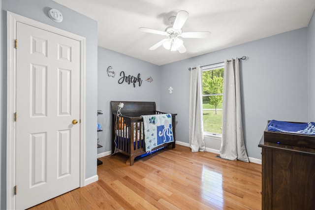 bedroom with baseboards, a crib, ceiling fan, and light wood-style floors