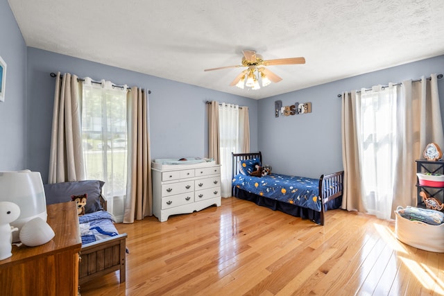 bedroom with light wood-type flooring, a textured ceiling, and ceiling fan