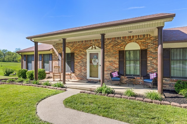 property entrance with a porch, a lawn, roof with shingles, and brick siding