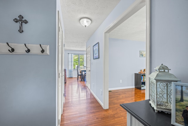hall featuring baseboards, a textured ceiling, and wood finished floors