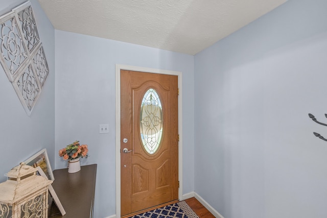 foyer entrance featuring baseboards, a textured ceiling, and wood finished floors