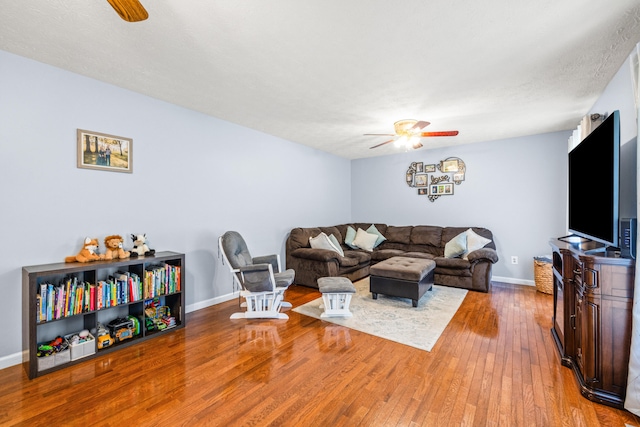 living area featuring baseboards, wood-type flooring, and a ceiling fan