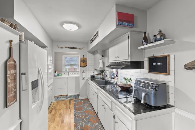 kitchen featuring washer and dryer, a sink, white cabinets, tasteful backsplash, and white appliances