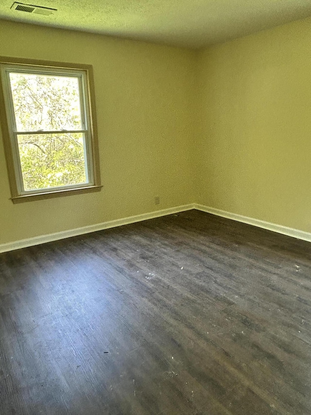 empty room featuring visible vents, dark wood-style flooring, and baseboards