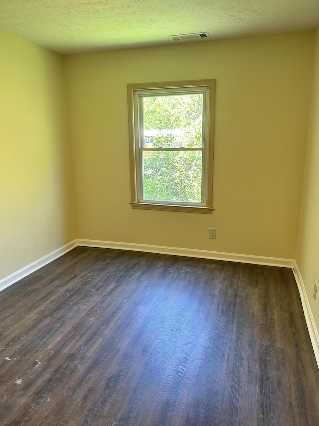 empty room featuring baseboards, visible vents, and dark wood-style flooring