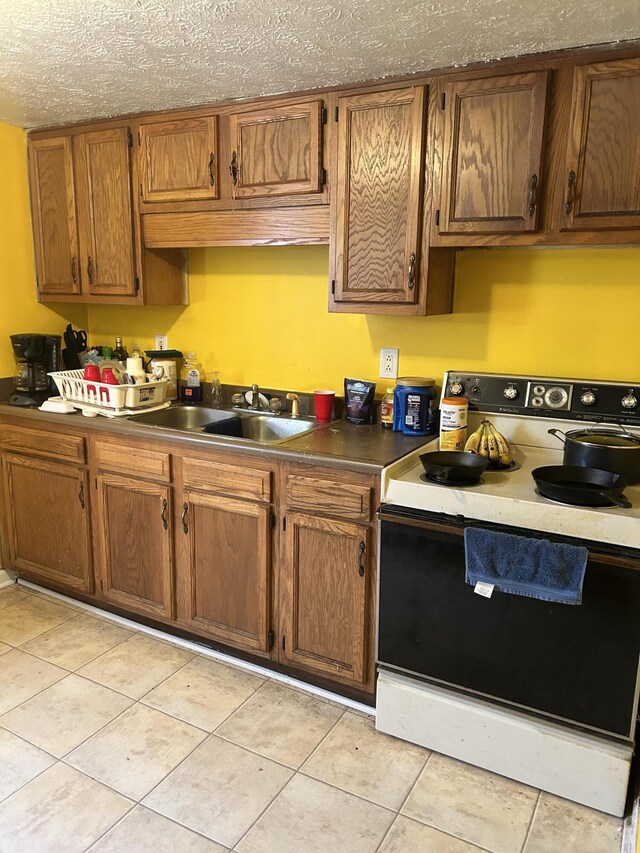 kitchen with a sink, white range with electric stovetop, light tile patterned floors, brown cabinetry, and dark countertops