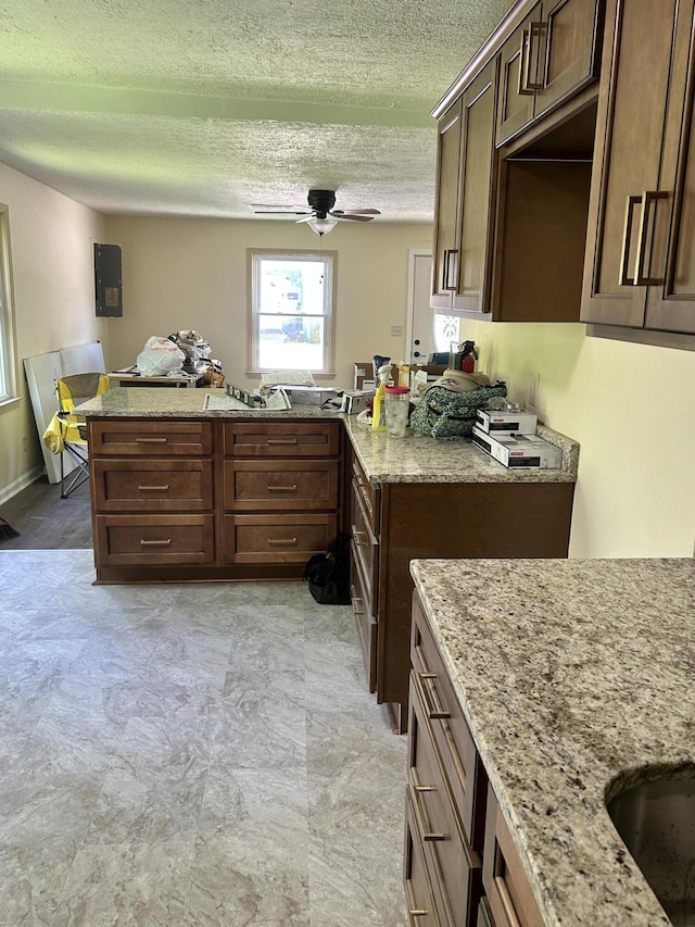 kitchen with dark brown cabinets, ceiling fan, a textured ceiling, and light stone counters
