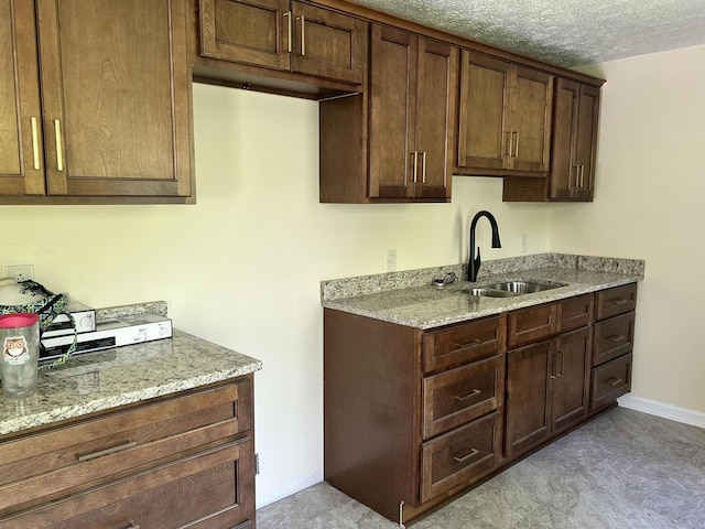 kitchen with light stone counters, a textured ceiling, dark brown cabinets, and a sink