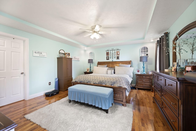 bedroom featuring baseboards, a ceiling fan, a tray ceiling, and wood finished floors