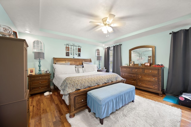 bedroom with light wood finished floors, ceiling fan, and a tray ceiling