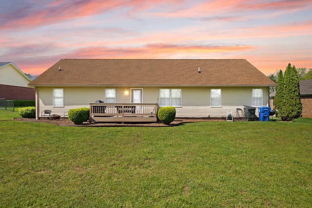 back of house featuring roof with shingles, a yard, and a deck