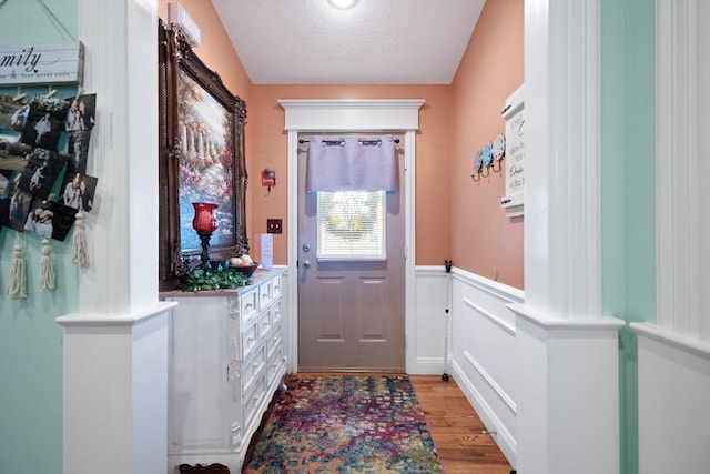 doorway with wainscoting, light wood-type flooring, and a textured ceiling