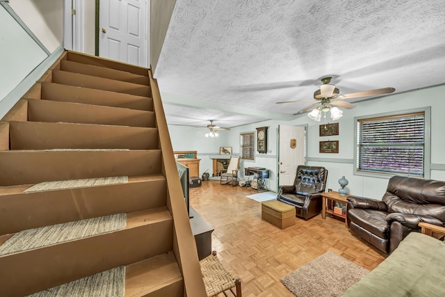 living room featuring stairway, ceiling fan, and a textured ceiling
