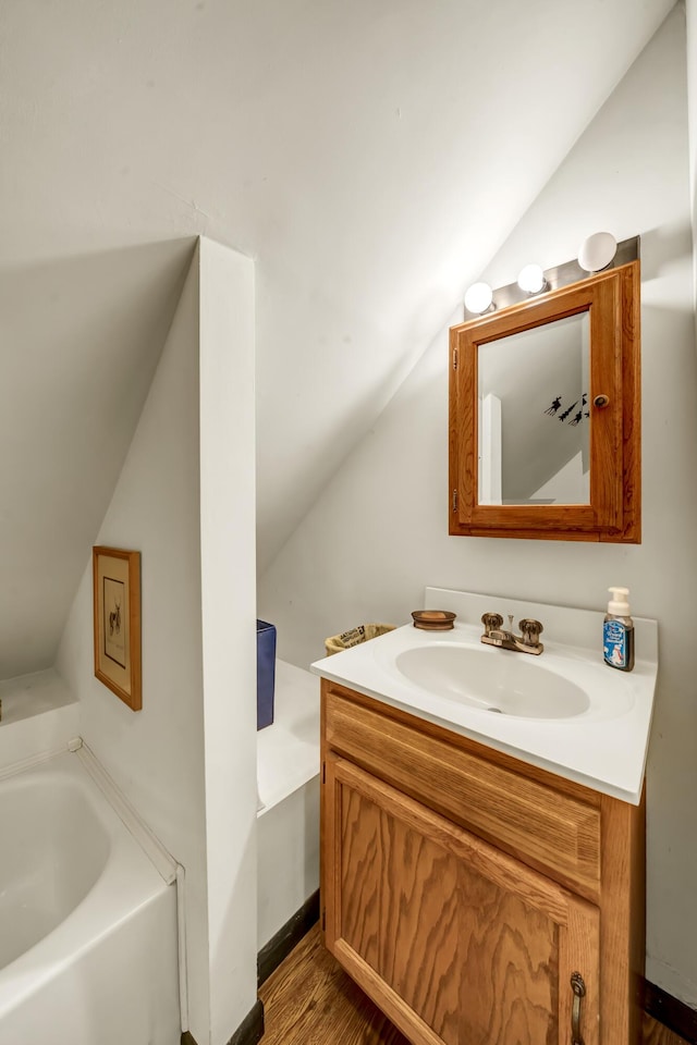 full bathroom with a garden tub, wood finished floors, vaulted ceiling, and vanity