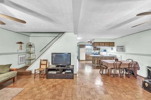 living area with stairs, a textured ceiling, ceiling fan, and a wall mounted air conditioner