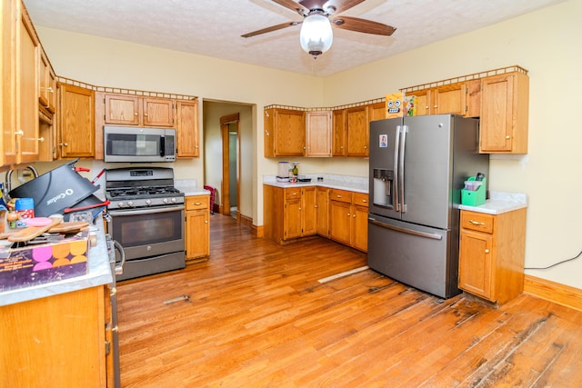 kitchen with stainless steel appliances, light wood-style flooring, light countertops, baseboards, and ceiling fan