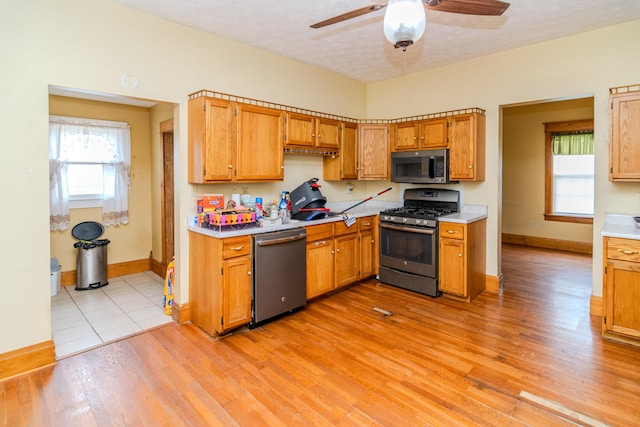 kitchen with appliances with stainless steel finishes, light countertops, baseboards, a ceiling fan, and light wood-style floors