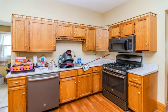 kitchen featuring dishwashing machine, stainless steel range with gas cooktop, light countertops, a sink, and light wood-style floors