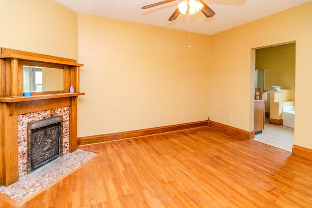 unfurnished living room with wood finished floors, a fireplace, a ceiling fan, and baseboards