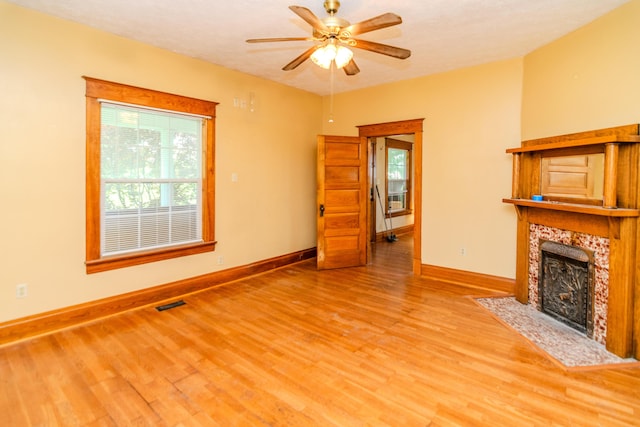 unfurnished living room with light wood-style floors, baseboards, a fireplace, and a ceiling fan