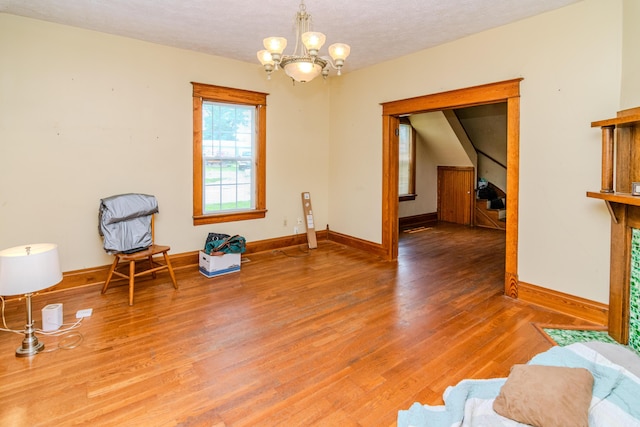 living area with a chandelier, light wood-type flooring, baseboards, and a textured ceiling
