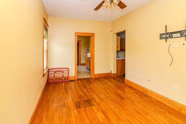 empty room with ceiling fan, light wood finished floors, and baseboards