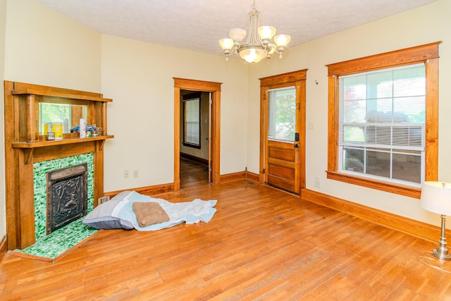 foyer featuring baseboards, wood finished floors, a chandelier, a tile fireplace, and a textured ceiling
