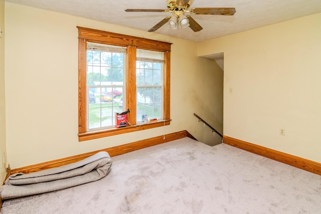 carpeted empty room featuring baseboards, a ceiling fan, and a textured ceiling