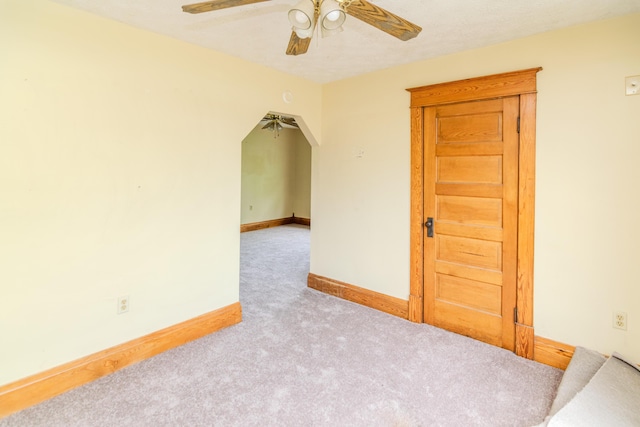 carpeted empty room with ceiling fan, baseboards, and arched walkways