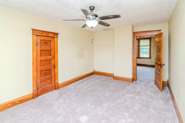 unfurnished room with ceiling fan, light carpet, a textured ceiling, and baseboards
