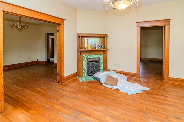unfurnished living room featuring a chandelier, wood finished floors, a tiled fireplace, and baseboards