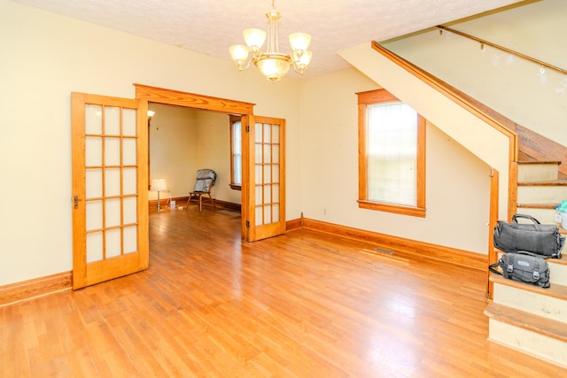 unfurnished living room with french doors, a textured ceiling, light wood-style floors, stairway, and a chandelier