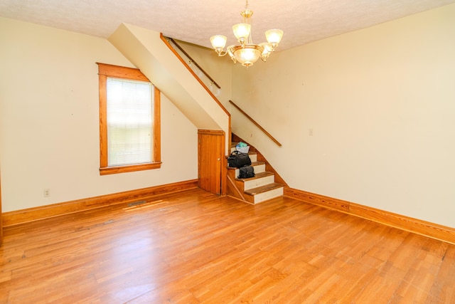 unfurnished living room featuring stairs, light wood-style floors, a chandelier, baseboards, and a textured ceiling