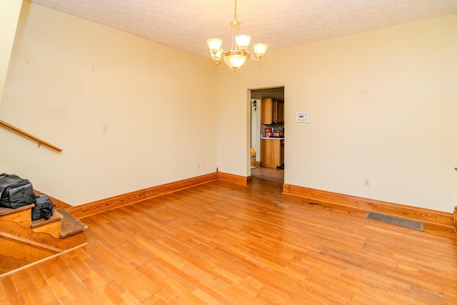 unfurnished living room featuring light wood-style flooring, a chandelier, baseboards, and a textured ceiling