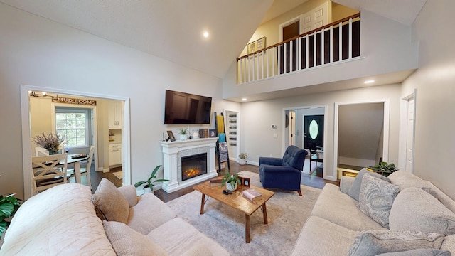 living area with light wood-style floors, baseboards, a glass covered fireplace, recessed lighting, and high vaulted ceiling