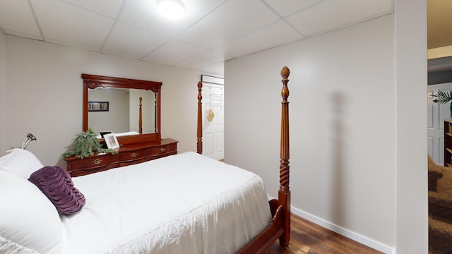 bedroom featuring baseboards, wood finished floors, and a paneled ceiling
